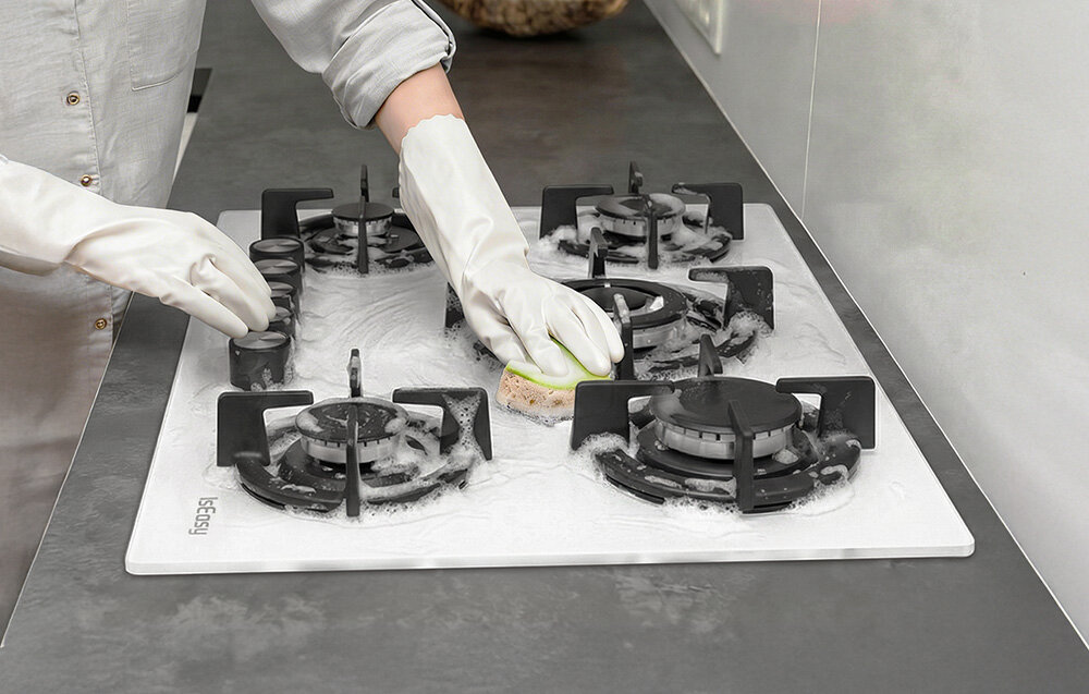 Płyta gazowa ISEASY MGBG-775 Osoba czyści płytę gazową, pokrytą pianą, używając gąbki i rękawic ochronnych. Ujęcie podkreśla łatwość utrzymania powierzchni i rusztów w czystości szkło czyszczenie wilgotna ściereczka estetyka higiena