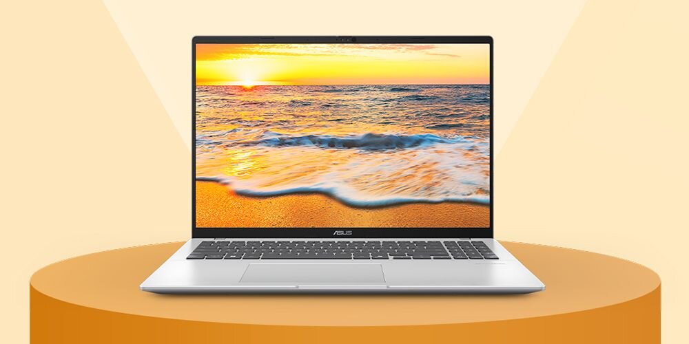 Laptop z wyświetlaczem pokazującym obraz plaży z zachodzącym słońcem. Na obudowie widoczne jest logo ASUS.
