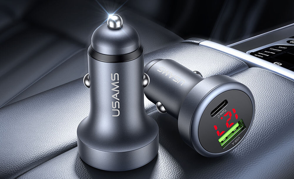 Szara ładowarka samochodowa z logo USAMS, posiadająca dwa porty USB i wyświetlacz cyfrowy pokazujący napięcie 12V.