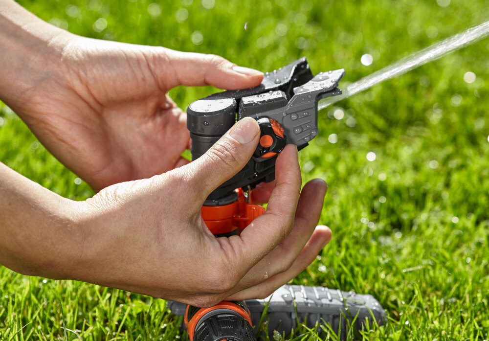 Zraszacz GARDENA Comfort na szpilce 8144-20 ogród trawnik zraszacz na trawniku osoba trzyma w palcach pokrętło do regulacji pierścienie regulacyjne sektor nawadniania w zakresie od 25° do 360 wybrany kąt łatwo odczytasz na oznaczeniach pierścieni oszczędza wodę efektywność podlewania