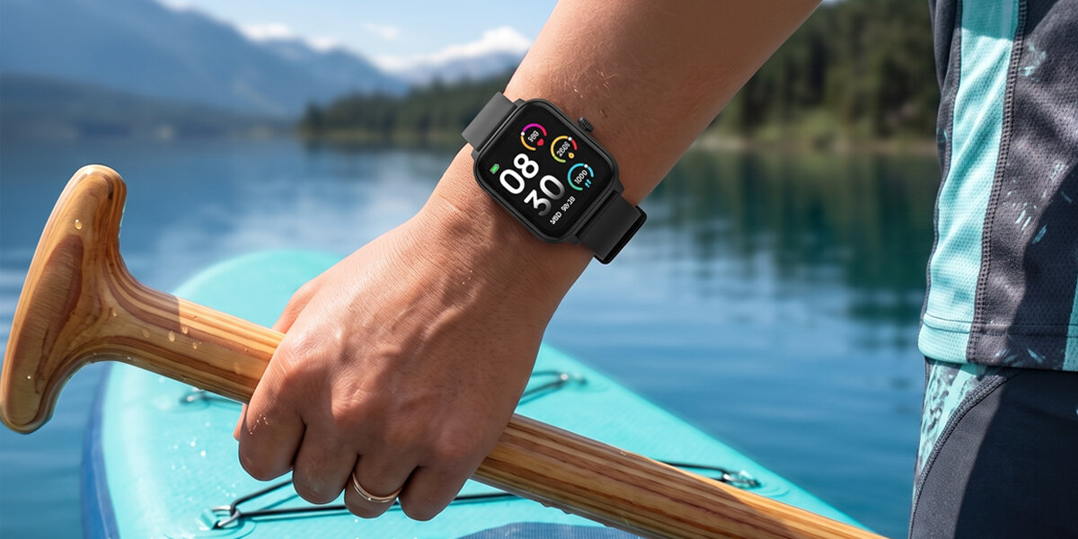 Mężczyzna trzyma drewniane wiosło na tle jeziora i gór. Na nadgarstku znajduje się czarny, prostokątny smartwatch Denver.