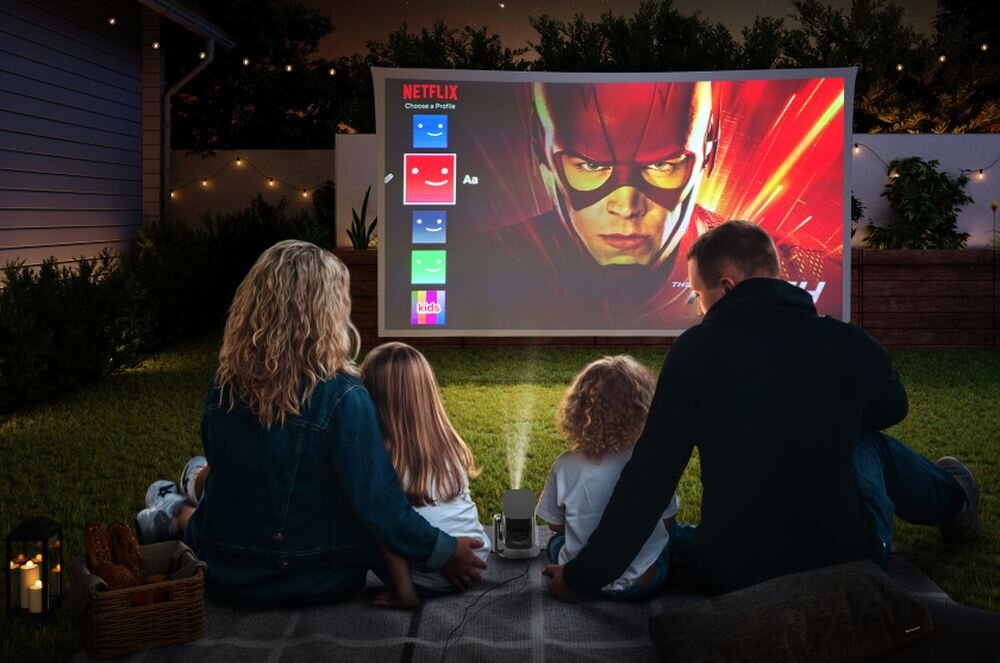 Projektor XGIMI MoGo 2 Pro GTV Google TV Netflix YouTube Google Cast Asystent Google, projektor stojący na kocu w plenerze wyświetlający obraz na ekranie projekcyjnym