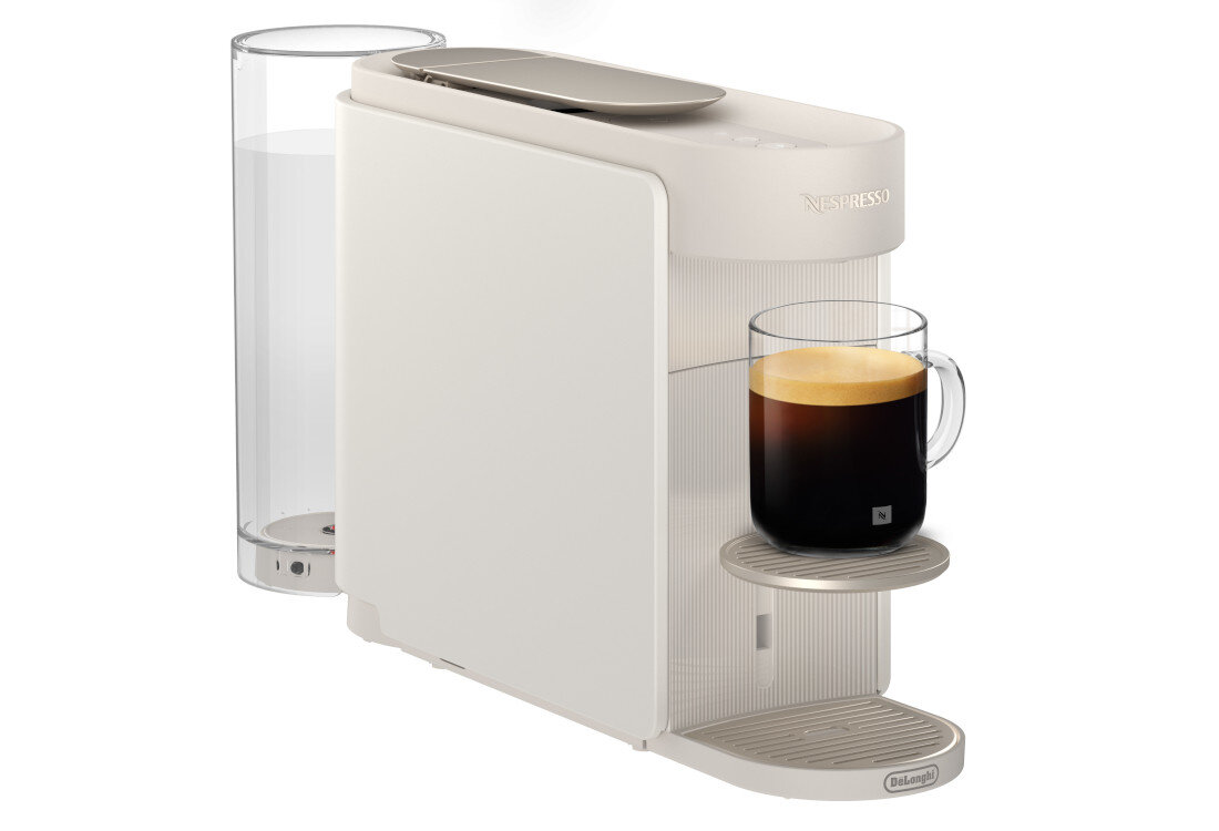 Biały ekspres do kawy z przezroczystym pojemnikiem na wodę i filiżanką z kawą na podstawce. Widoczne logo \'Nespresso\' i \'DeLonghi\'.