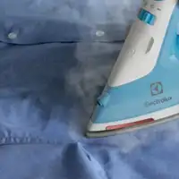 Żelazko w kolorze niebiesko-białym prasuje niebieską koszulę, wydobywa się z niego para. Na żelazku widoczne jest logo producenta.