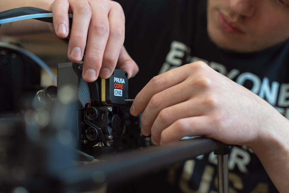 Drukarka 3D PRUSA Core One+ Wi-Fi, LAN + Zestaw do montażu Zbliżenie na dłonie osoby montującego głowicę drukującą Nextruder, czujnik tensometryczny, autokalibracja