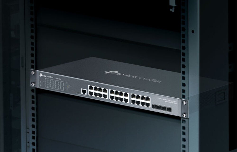 Switch TP-LINK Omada SG3428X Przełącznik sieciowy zamontowany w ciemnej metalowej szafie serwerowej Rack widoczny od przodu w oświetleniu punktowym, opis