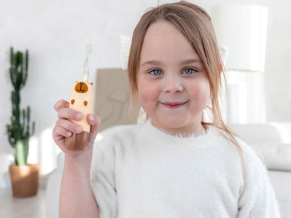 Szczoteczka soniczna dla dzieci INNOGIO GIO-454 kapibara Uśmiechnięta dziewczynka trzymająca szczoteczkę soniczną dla dzieci InnoGIO GIOcapybara w kształcie kapibary.