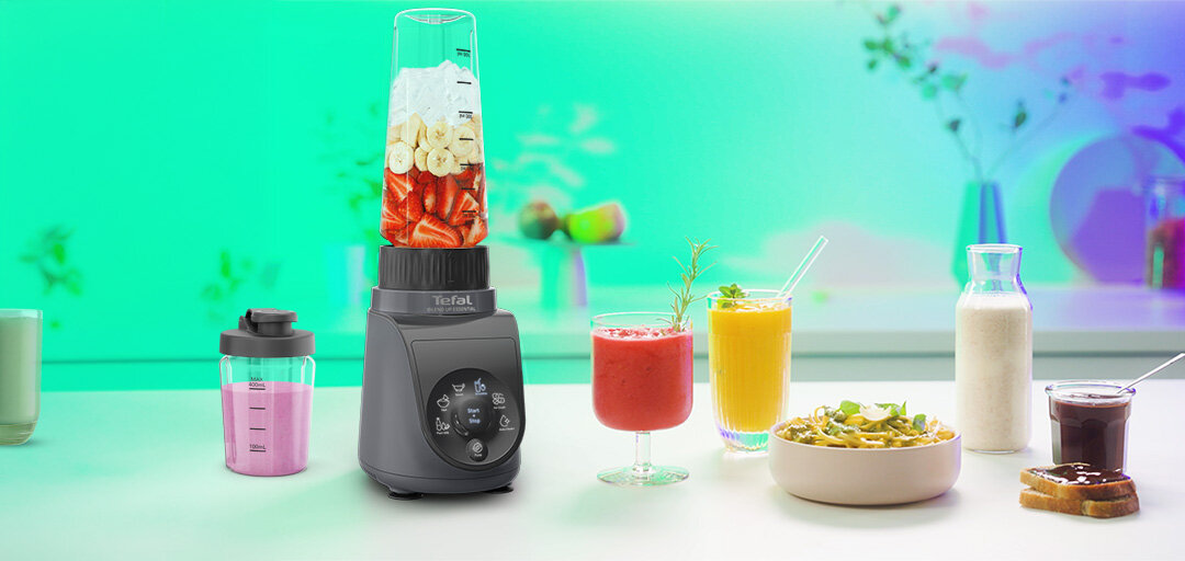 Na blacie kuchennym znajduje się blender z logo \'Tefal\', wypełniony owocami. Obok niego stoją różne napoje i przekąski w szklankach i miseczkach.