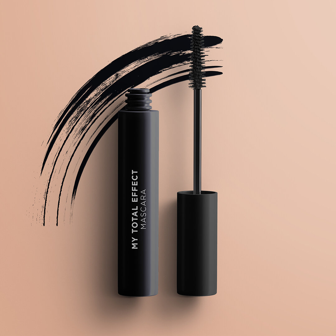 Czarny tusz do rzęs z napisem \'MY TOTAL EFFECT MASCARA\' na tle beżowej powierzchni, obok widoczny jest pędzelek z tuszem oraz ślad pociągnięcia tuszem.