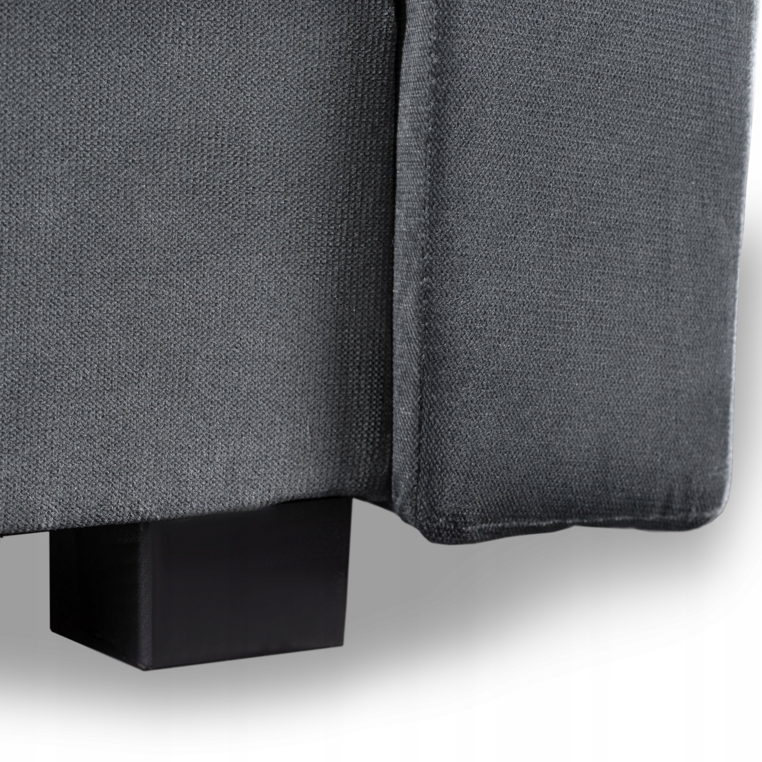 Fragment szarej kanapy z widoczną teksturą materiału i czarną, prostokątną nogą.