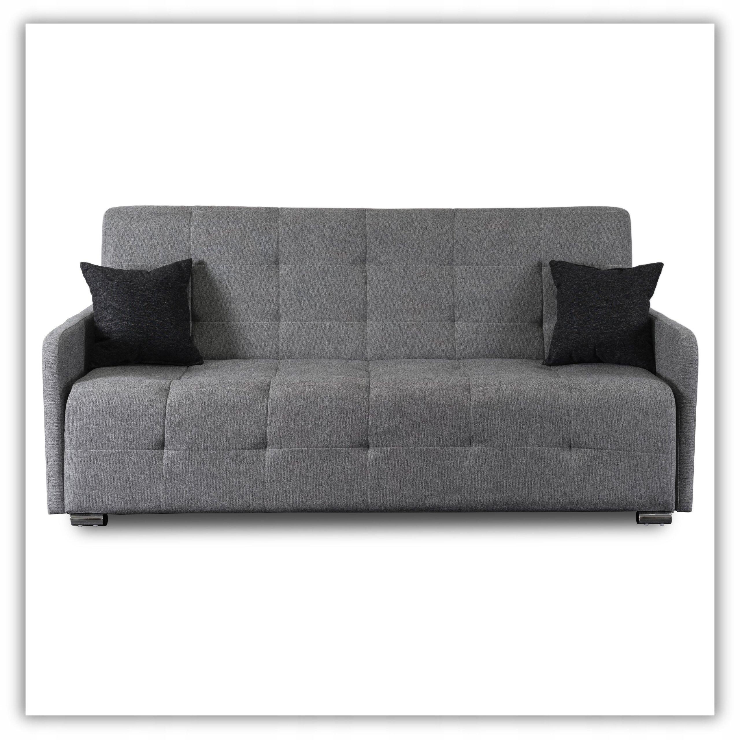 Szara, rozkładana sofa z funkcją spania, z dwoma czarnymi poduszkami. Sofa ma prosty, nowoczesny design z widocznymi przeszyciami na oparciu i siedzisku.