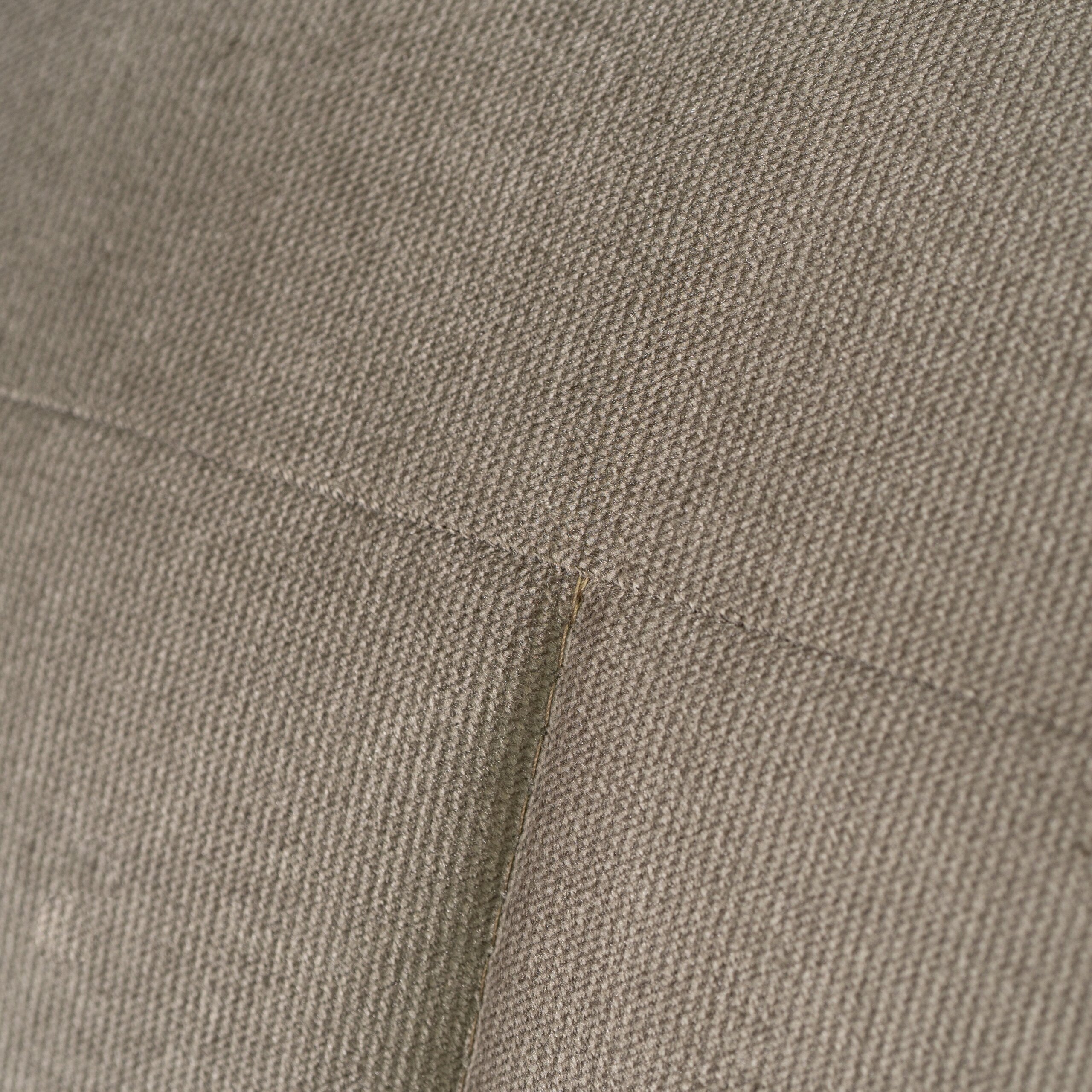 Zbliżenie na beżowy materiał o teksturze tkaniny z widocznym szwem.