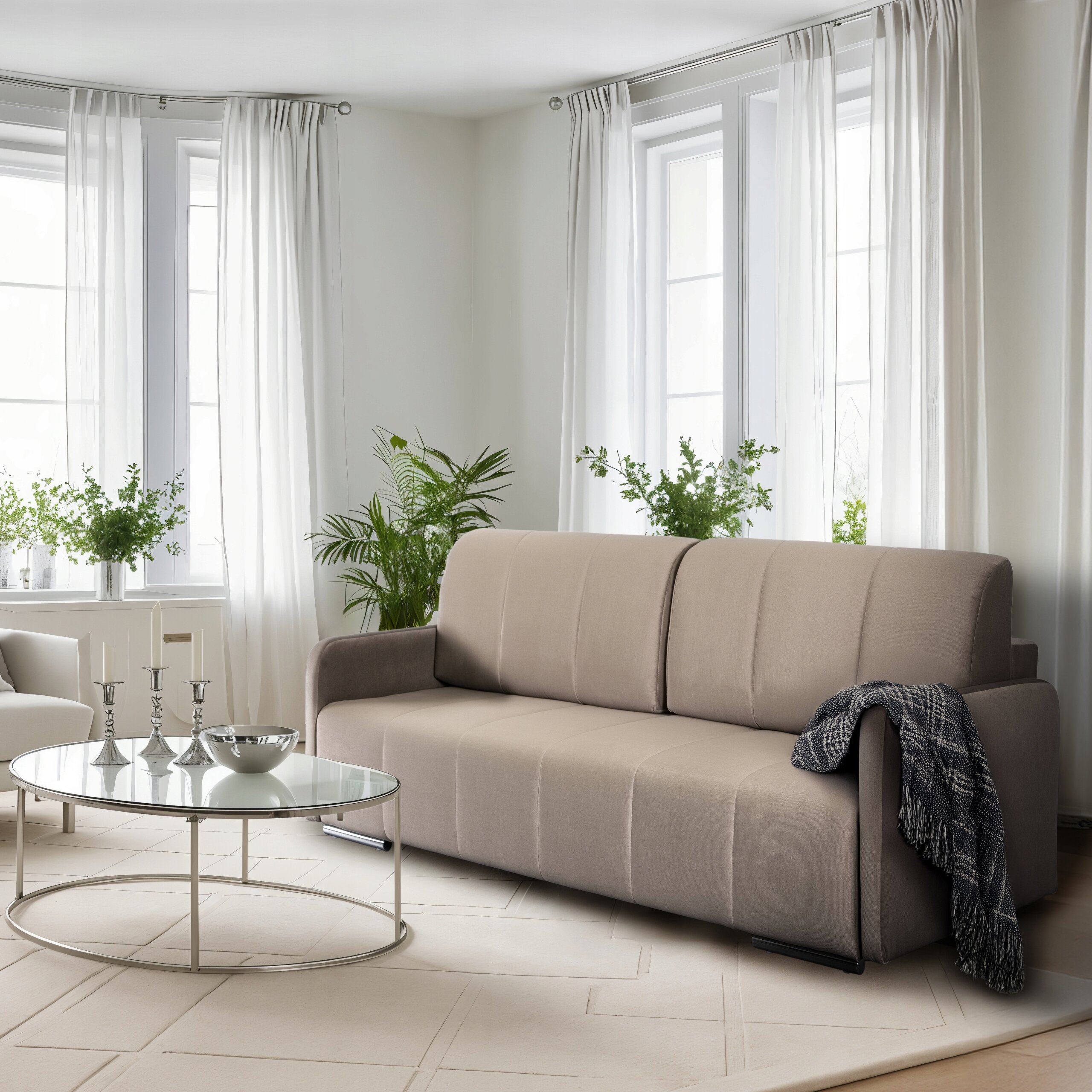 Beżowa sofa rozkładana z funkcją spania stoi w jasnym pokoju z trzema dużymi oknami i białymi zasłonami. Przed sofą znajduje się okrągły stolik z metalowymi nogami, na którym stoją trzy świeczniki i miska.