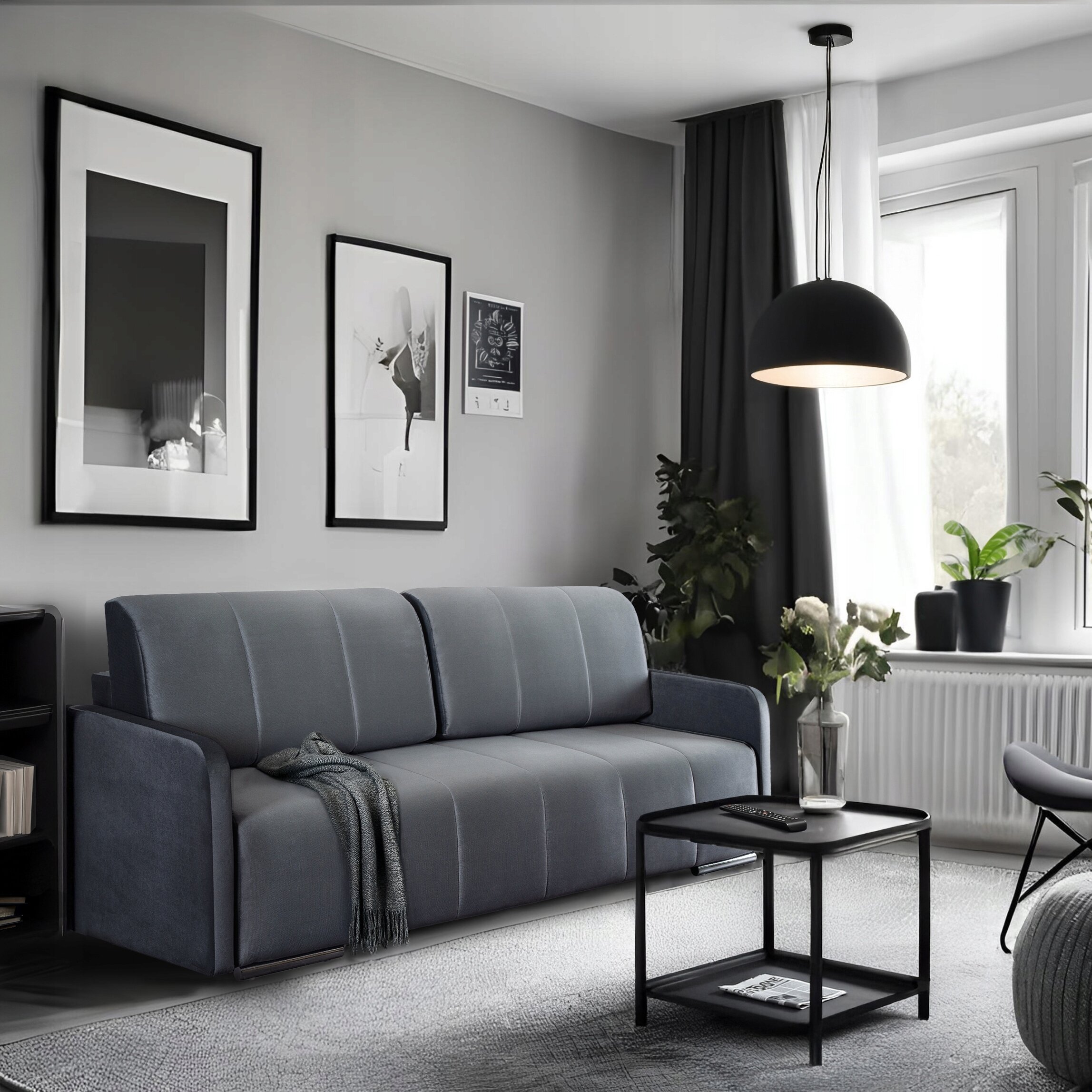 Szara, rozkładana sofa dwuosobowa stoi w nowoczesnym salonie z jasnymi ścianami i dużym oknem. Na ścianie wiszą trzy czarno-białe obrazy, a obok sofy znajduje się czarny stolik z wazonem pełnym kwiatów.