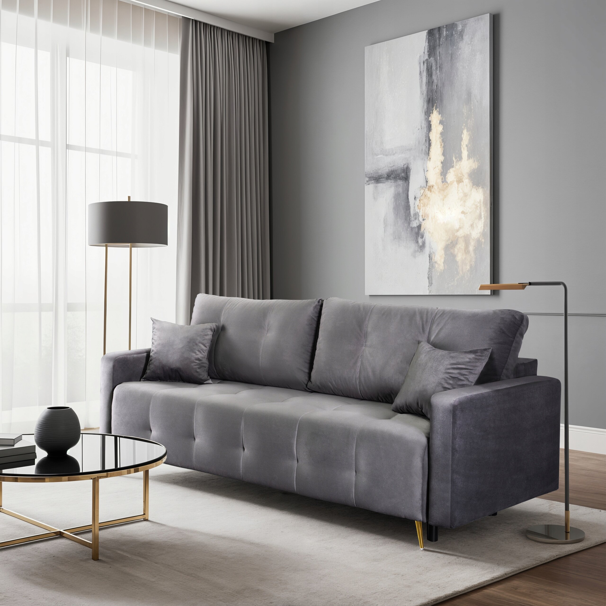 Szara sofa rozkładana z funkcją spania stoi w eleganckim salonie z szarymi ścianami i dużym oknem z zasłonami. Obok sofy znajduje się okrągły stolik z czarnym blatem i złotymi nogami oraz lampa podłogowa.