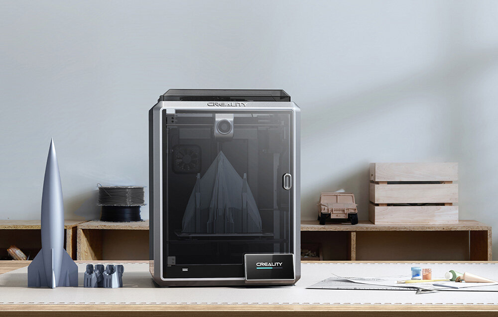 CREALITY K1 drukarka na blacie obok widoczne wydruki oraz skrzynka