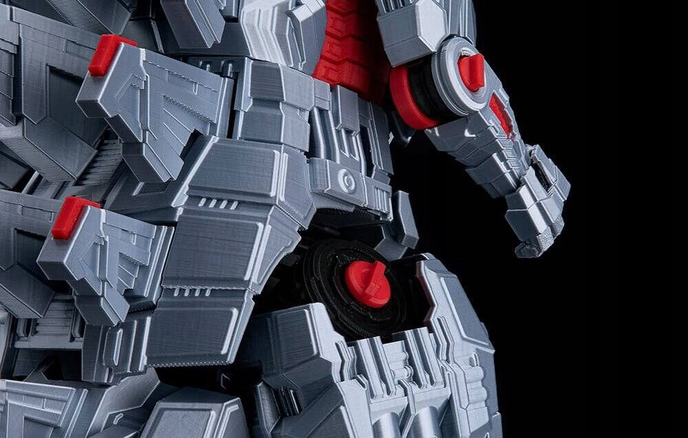 Fragment szarej, mechanicznej konstrukcji z czerwonymi elementami, przypominający część robota lub maszyny.