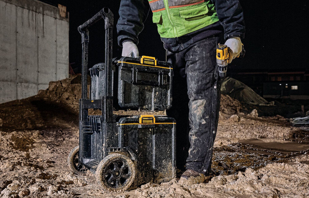 Skrzynka narzędziowa DEWALT DS450 plac budowy osoba ustawia skrzynię jedną na drugą obudowa z tworzywa sztucznego odporna na uszkodzenia mechaniczne i działanie czynników zewnętrznych metalowe zatrzaski i metalowe zawiasy udźwig do 70 kg