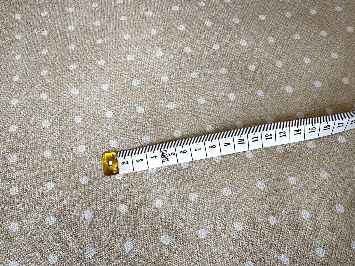 Beżowa cerata w białe kropki z miarką krawiecką pokazującą długość do 17 cm.