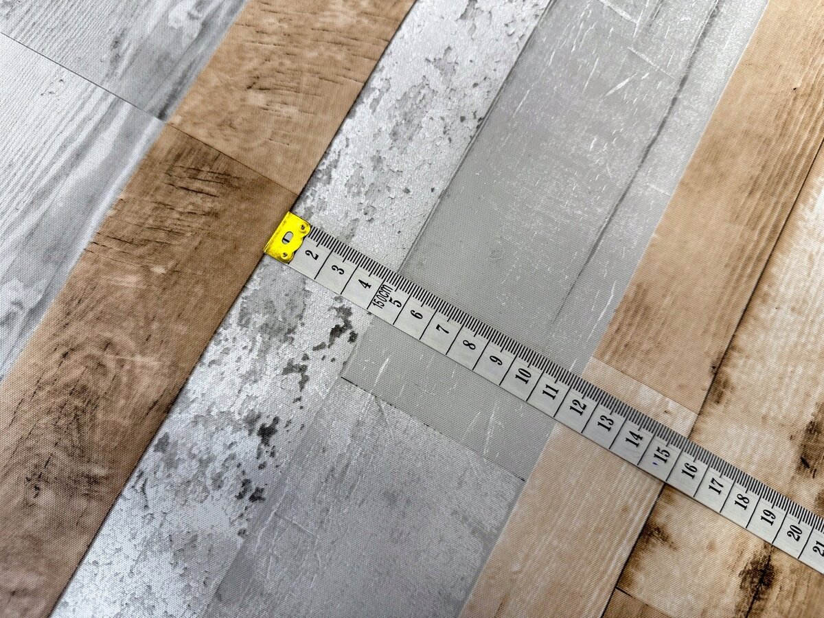 Obraz przedstawia fragment ceraty z wzorem imitującym drewno i beton, na której leży rozwinięta miarka z widocznymi centymetrami od 1 do 15.