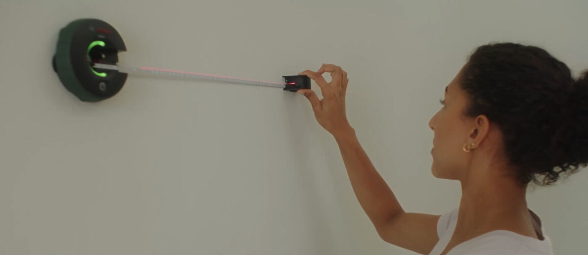 Laser liniowy BOSCH Atino 0603663A02 Edycja Limitowana, laser, miara, AA, galeria, kobieta odmierza laserek dystans na ścianie