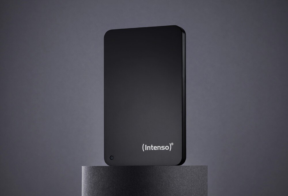 Dysk INTENSO Memory Case Prostokątny dysk zewnętrzny ustawiony pionowo na ciemnym, cylindrycznym podwyższeniu, z widocznym logotypem 'Intenso' oraz małą diodą w rogu, opis
