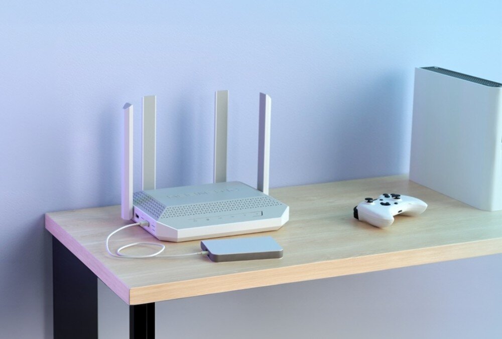 Router KEENETIC Titan 3 białe urządzenie sieciowe z czterema antenami stoi na jasnym drewnianym blacie obok konsoli do gier, kontrolera i małego dysku zewnętrznego podłączonego kablem