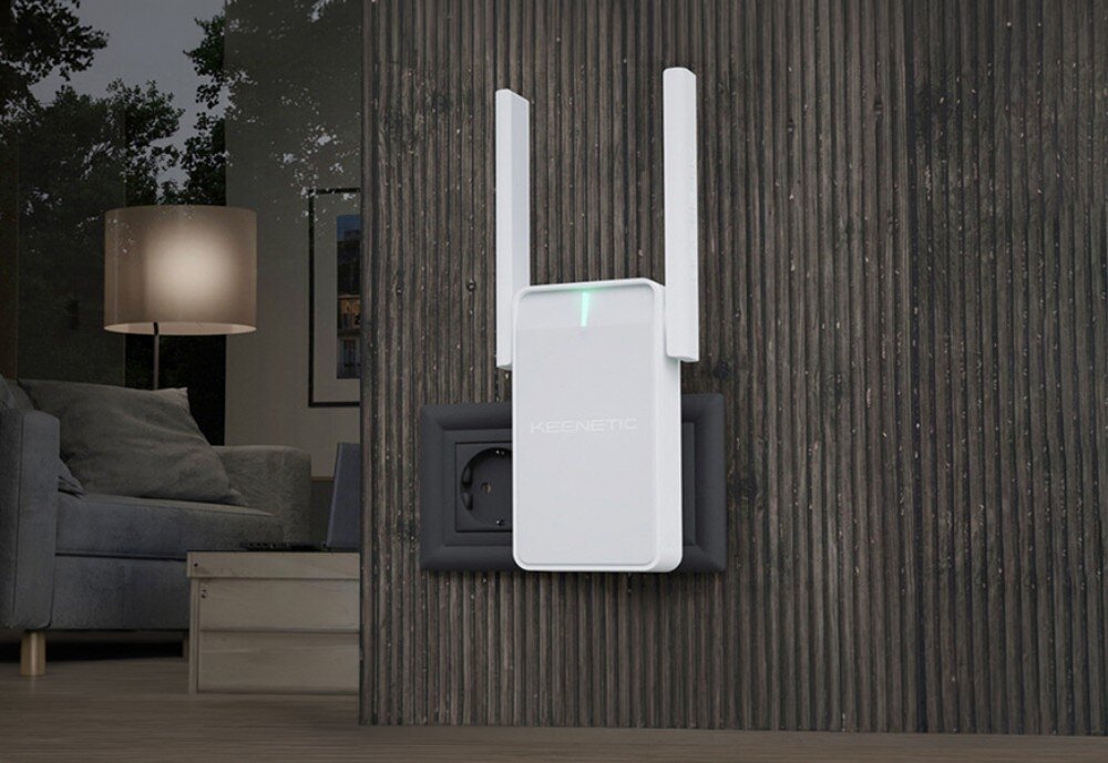 Wzmacniacz sieci KEENETIC Buddy 4 Kompaktowy wzmacniacz sygnału z dwiema antenami i świecącą diodą umieszczony w gniazdku na ścianie o strukturze ciemnego drewna w nowoczesnym salonie
