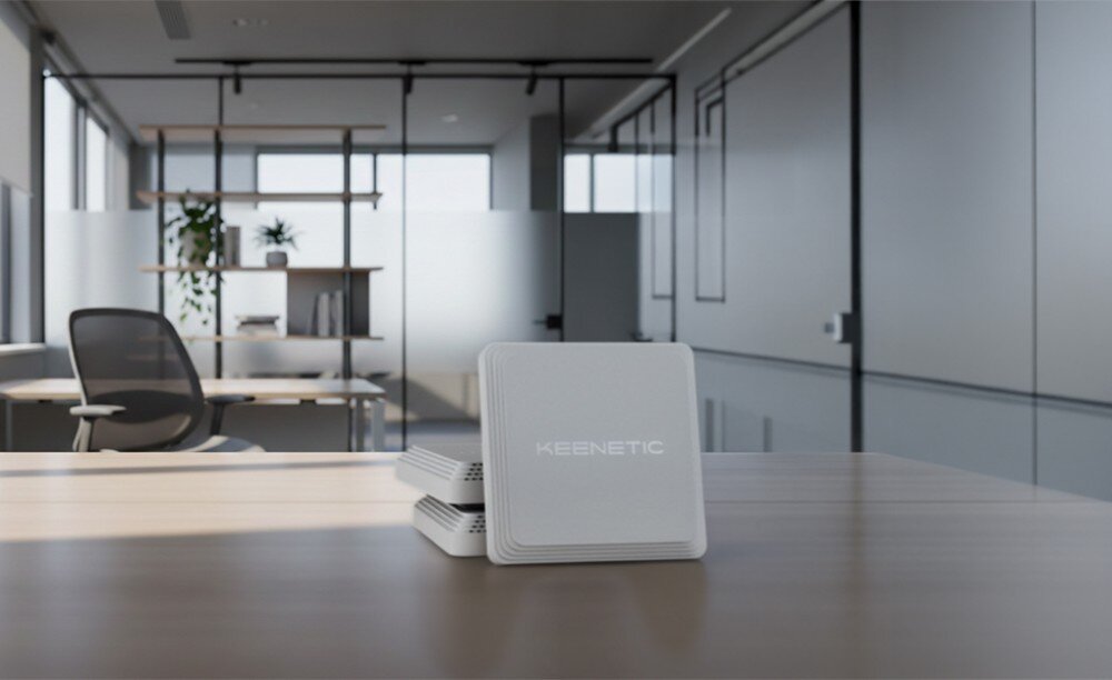 Punkt dostępu KEENETIC Voyager Pro Białe kwadratowe urządzenie ustawione na biurku w nowoczesnym biurze z widocznym w tle krzesłem i szklanymi ścianami