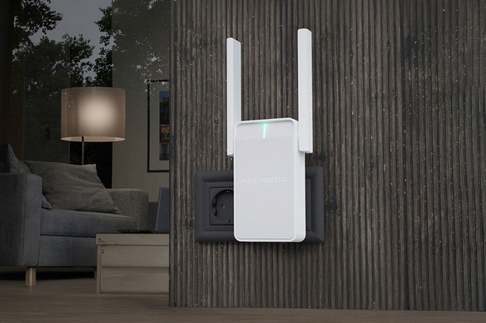 Wzmacniacz sieci KEENETIC Buddy 5 białe urządzenie z dwiema antenami i świecącą zieloną diodą wpięte do gniazdka na ciemnej ścianie o pionowej teksturze