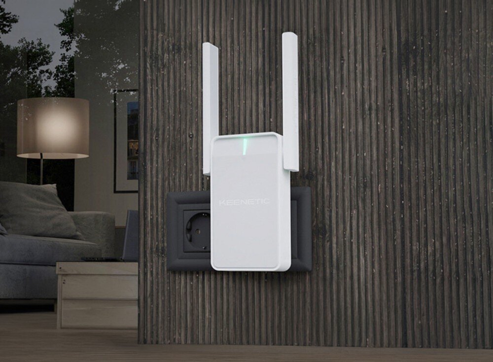 Wzmacniacz sieci KEENETIC Buddy 6 Biały wzmacniacz sygnału z dwiema antenami i świecącą zieloną diodą wpięty do gniazdka na ścianie z ciemnych listew