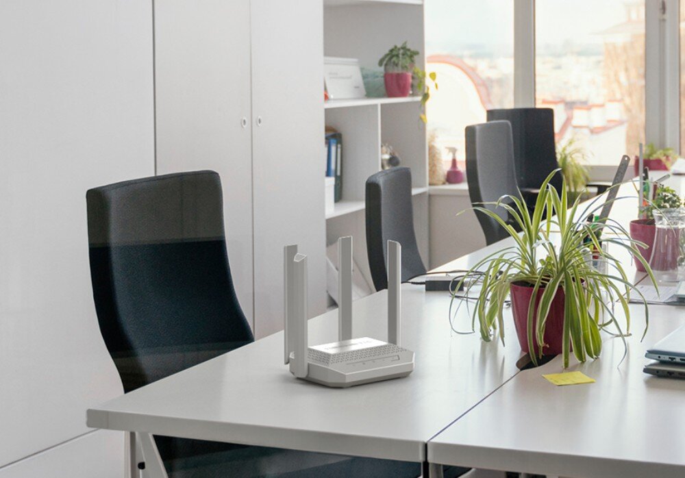 Router KEENETIC Speedster 4G+ Biały ruter z czterema antenami stoi na jasnym biurku w biurze obok czarnych krzeseł i rośliny doniczkowej