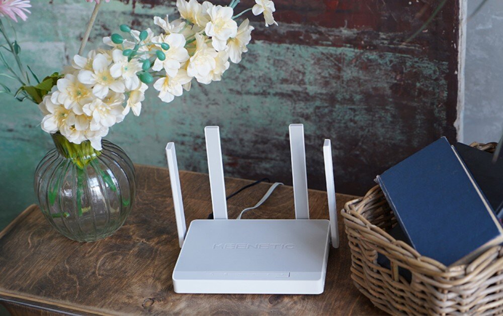 Router KEENETIC Hopper DSL Router z czterema antenami ustawiony centralnie na drewnianej powierzchni obok zielonej rośliny w białej doniczce na tle gładkiej, jasnej ściany