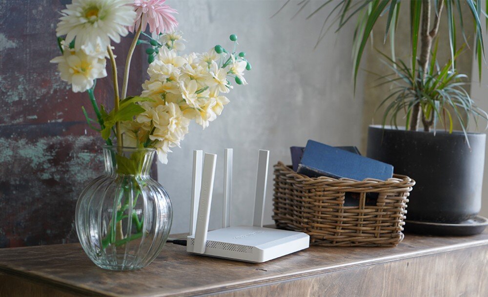 Router KEENETIC Hopper DSL Zbliżenie na biały router z czterema uniesionymi antenami stojący na jasnym meblu, w tle widać fragment szarej sofy i roślinę doniczkową