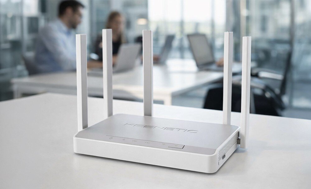 Router KEENETIC Hopper DSL Osoba w białej koszuli trzyma przed twarzą duże białe pudełko z grafiką i opisem technicznym routera, siedząc w żółtym fotelu obok wysokiej rośliny