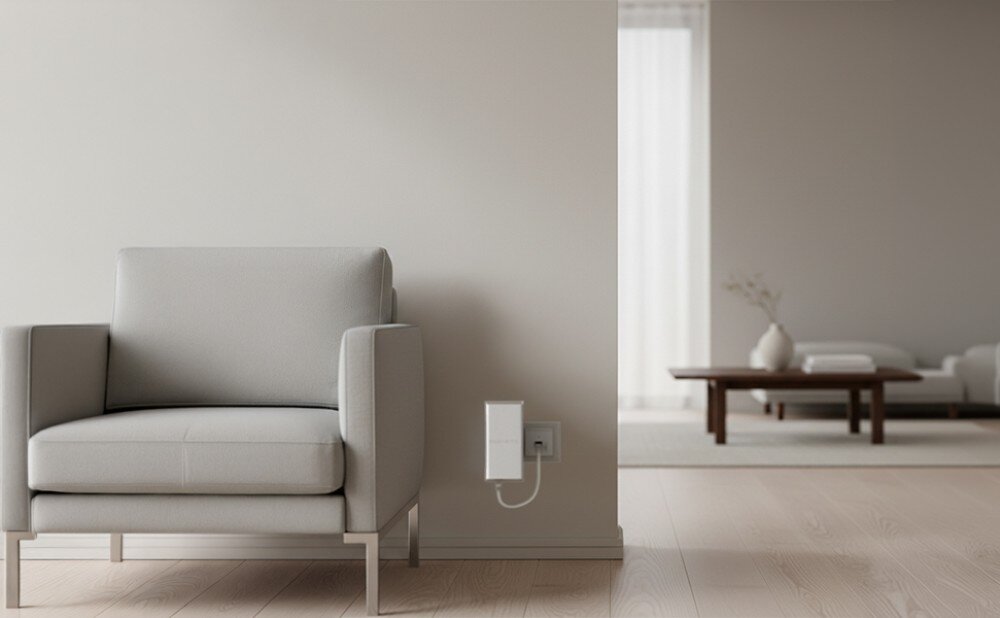 Wzmacniacz sieci KEENETIC Buddy 6 SE Biały moduł na jasnej ścianie obok szarego fotela, w tle widoczny salon z niskim stolikiem i kanapą