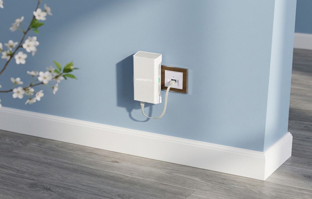 Wzmacniacz sieci KEENETIC Buddy 6 SE Białe urządzenie podłączone do gniazdka na niebieskiej ścianie nad białą listwą przypodłogową i drewnianą podłogą