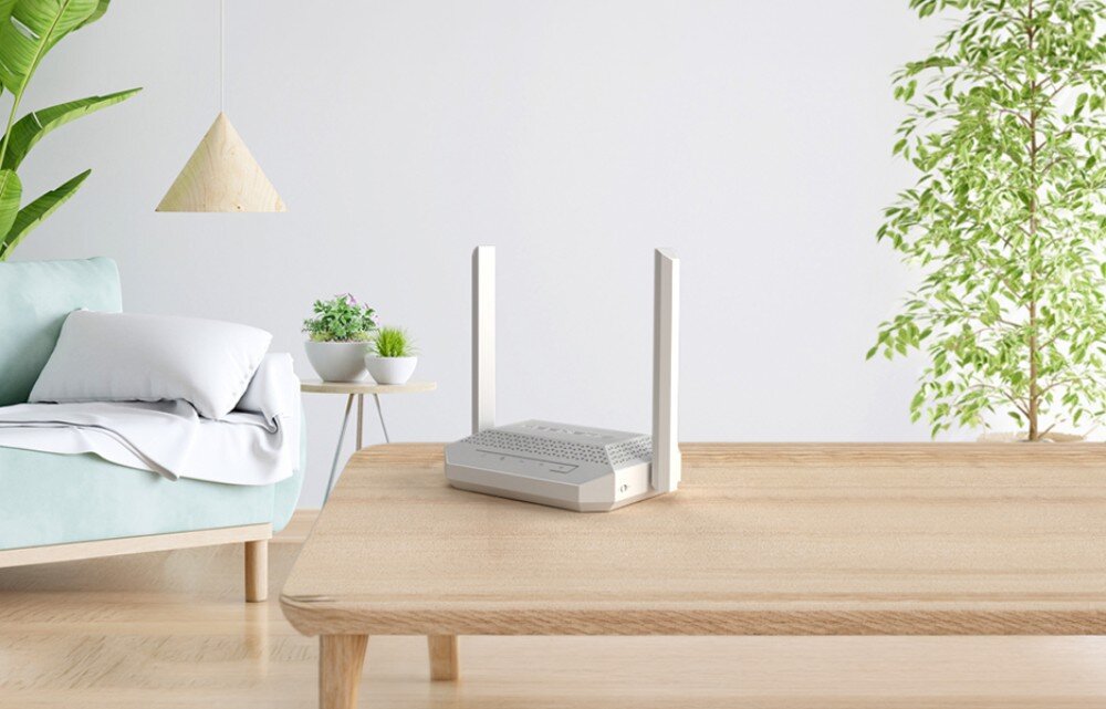Router KEENETIC Racer Urządzenie sieciowe z dwiema antenami umieszczone na drewnianym ławie w nowoczesnym salonie z miętową sofą, roślinami i wiszącą lampą