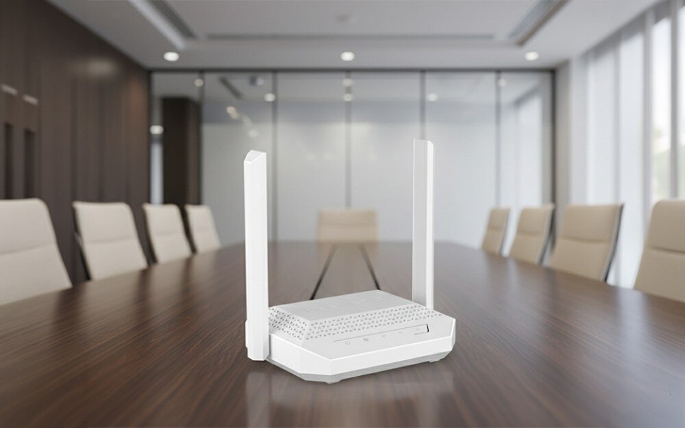 Router KEENETIC Racer Biały router z dwiema antenami stoi na środku długiego, ciemnego stołu w nowoczesnej sali konferencyjnej z rzędem jasnych krzeseł po bokach