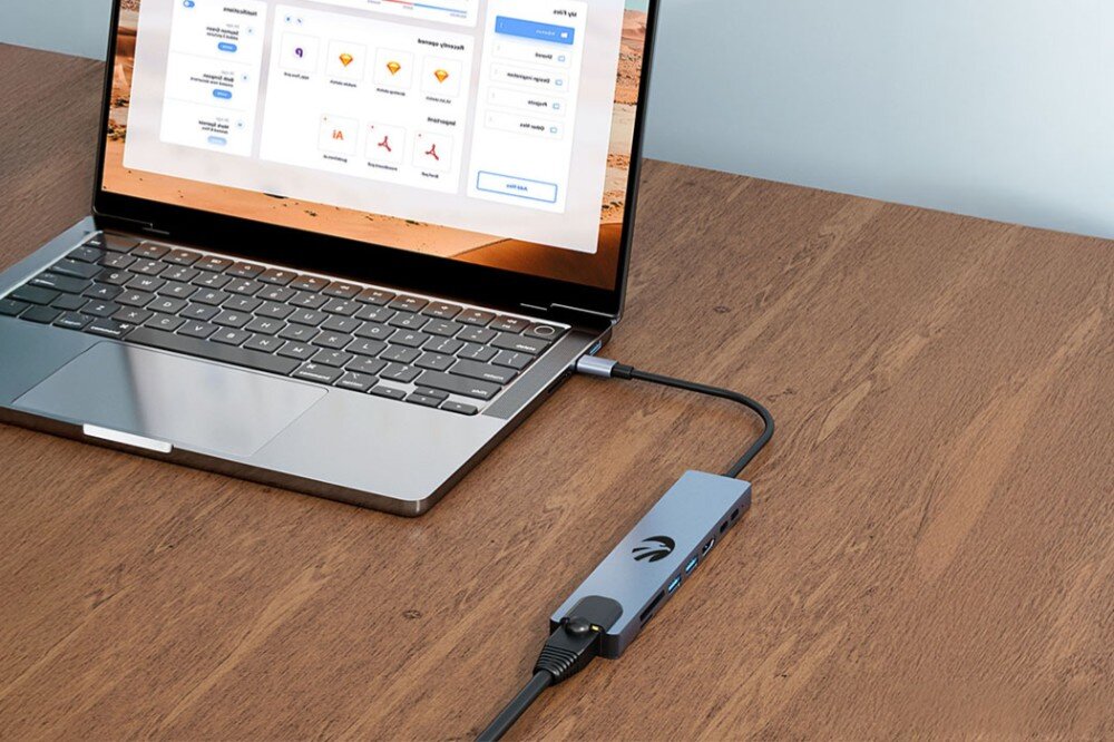 Hub HAWK HW-HUB801 8w1 Laptop na drewnianym biurku z podłączonym hubem. Do huba podłączony jest przewód Ethernet, złącze RJ-45, sieć, przepustowość