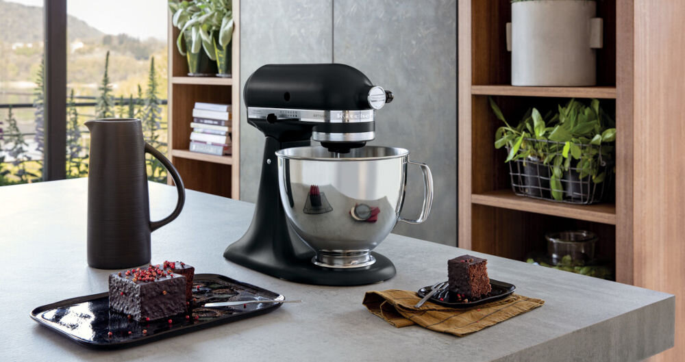 Robot kuchenny planetarny KITCHENAID Artisan 5KSM125EBM 300W kuchenny kompan robot czarna obudowa suwak srebrna misa robot stoi na blacie obok słodkości na talerzu 