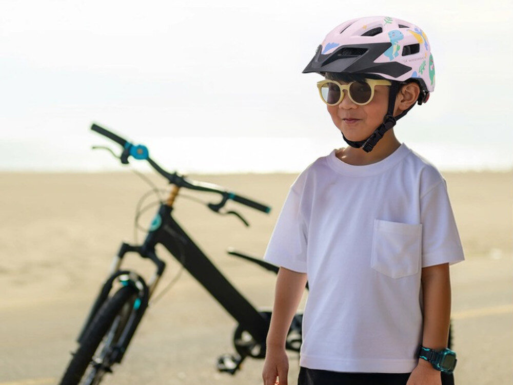 Kask rowerowy WOZINSKY HT-45R Różowy dla Dzieci (rozmiar XS), daszek, ochrona, słońce, wygoda, Chłopiec w kasku i okularach stoi na plaży obok roweru.