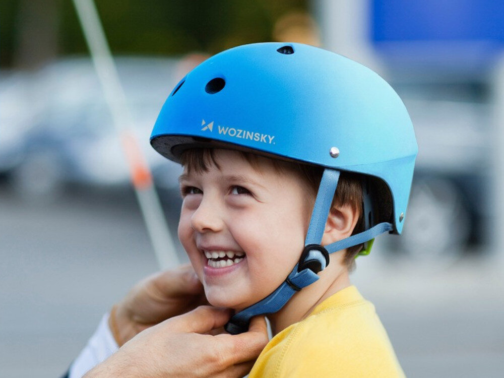 Dziecko nosi niebieski kask rowerowy z napisem \'WOZINSKY\'.