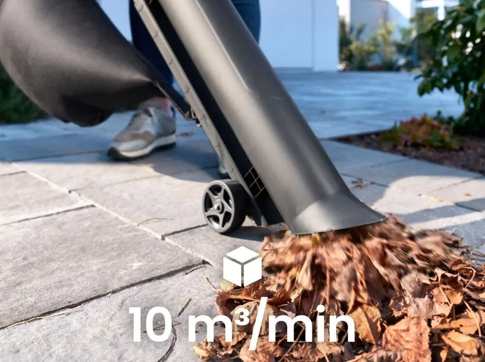 Osoba używa dmuchawy do liści, która wydmuchuje suche liście na chodniku. Na obrazie widoczny jest tekst: \'10 m³/min\'.