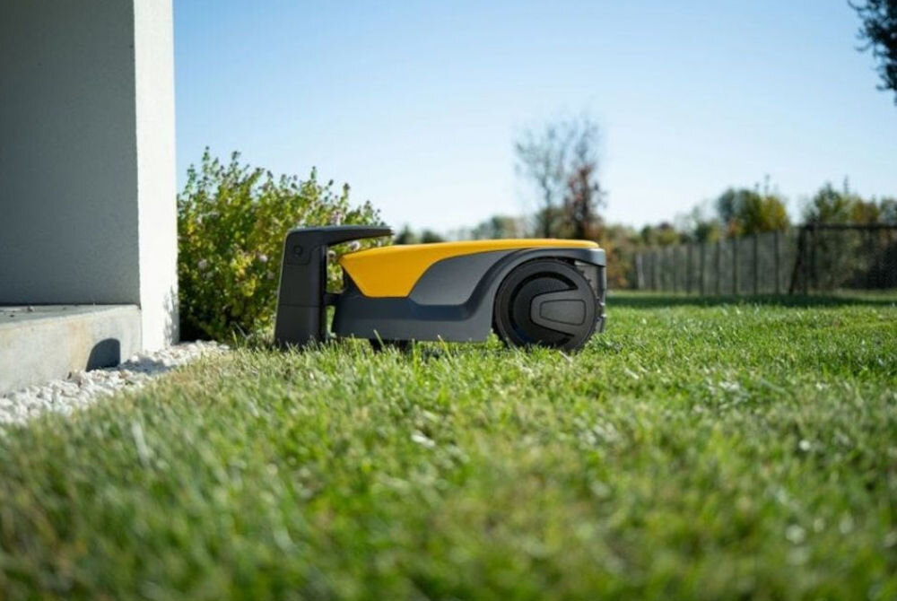 Robot koszący STIGA A 15V Bez przewodu ograniczającego Bluetooth 1500 m2, stacja, montaż, zasilacz, robot, Widok z boku na robota koszącego STIGA stojącego przy ścianie budynku na trawniku.