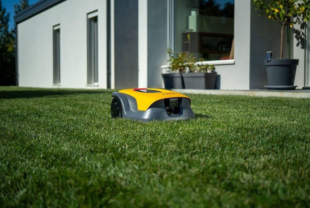 Robot koszący STIGA A 10V Bez przewodu ograniczającego Bluetooth 1000 m2, robot koszący, kosiarka, ogród, trawnik, Żółto-szary robot koszący STIGA na zadbanym trawniku przed domem.
