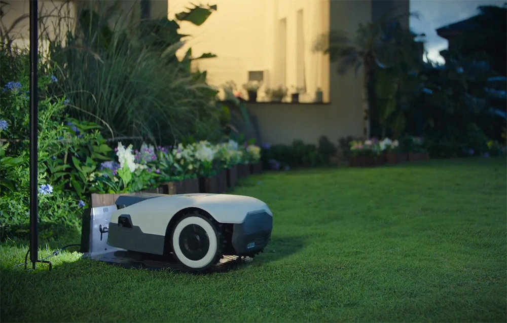 Robot koszący ANTHBOT Genie 800 Bez przewodu ograniczającego noc trawnik robot stoi w stacji ładującej w tle dom rośliny obudowa o klasie IPX6 przed wodą tworzywo sztuczne odporne na wilgoć kontakt z trawą drobne zabrudzenia może działać przez cały sezon ogrodowy