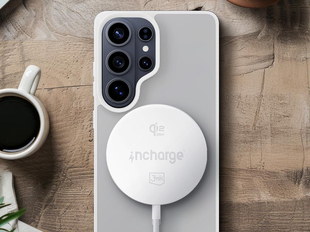 Na drewnianym stole leży telefon z dużym aparatem fotograficznym, na którym umieszczona jest biała ładowarka indukcyjna z napisami \'qi2 25W\', \'incharge\' i \'3mk\'. Obok telefonu znajduje się filiżanka z czarną kawą.