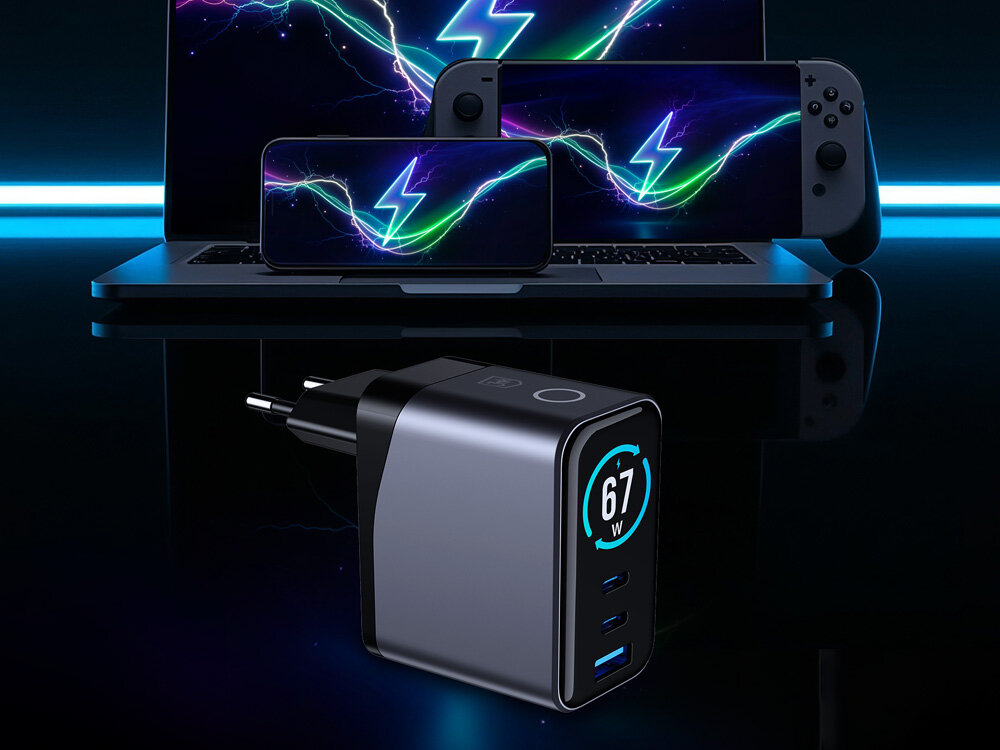 Kompaktowa ładowarka wieloportowa 67W obok laptopa, smartfona i konsoli do gier.