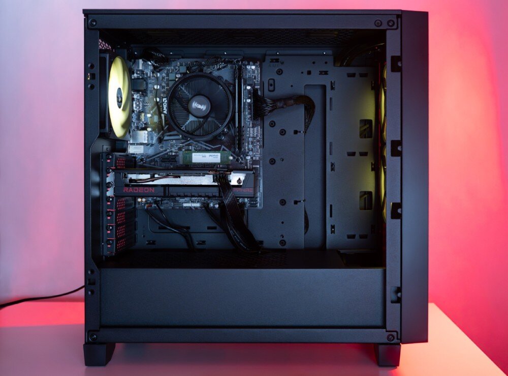 Obraz przedstawia wnętrze obudowy komputera z widocznymi komponentami, takimi jak karta graficzna z napisem \'Radeon\' i wentylator z logo \'AMD\'. W tle widoczne jest czerwone oświetlenie.